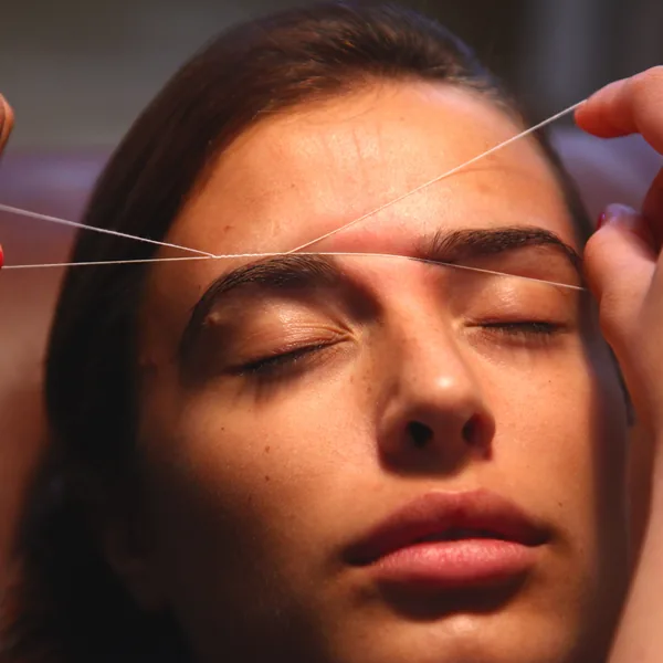 Threading in progress — the thread held taut across the brow